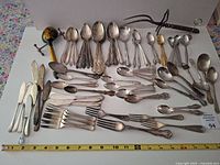 Full layout of mixed flatware and utensils with tape measure for scale