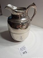 Front view of silver-plate Thermos jug showing handle, spout, reflective finish