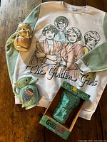 Group shot of sweatshirt, fish figurine, tan tiki figurine, boxed mug