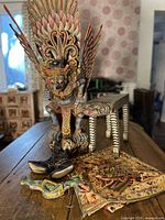 Garuda statue on zebra stool with textile panel and carved fragments visible