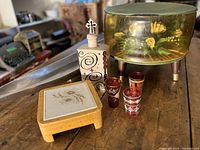 All items grouped on table: resin footstool, decanter, trivet, four shot glasses