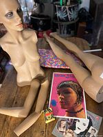 Mannequin torso, detached limbs, pop art print, small block, floral-covered ironing board top visible