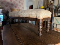 Side view of footstool showing upholstery and turned legs