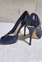 Angled rear and side view of both pumps showing patent finish, heel height and gold-tone plaque