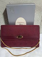 Front view of maroon Dior clutch with chain and box
