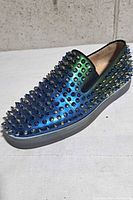 Left side view of single sneaker showing metallic blue-green finish and spikes