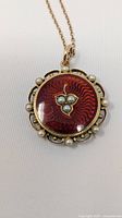 Close view of red enamel pendant with seed pearls and scalloped gold border