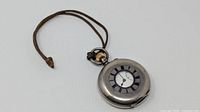 Closed pocket watch with leather cord showing blue enamel Roman numeral aperture