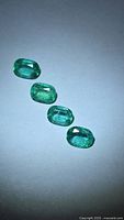 Four cushion-cut emeralds on light background