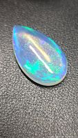 Pear cabochon opal on textured background showing play-of-color