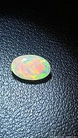 Oval faceted opal showing green and yellow fire on dark background