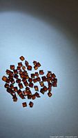 Pile of small red-orange square-cut garnets on white background