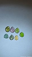 Seven tourmalines in array showing color variety and leaf carving
