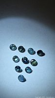 Ten small round blue-green sapphires arranged on white background under spotlight