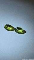 Pair of oval peridot gemstones on neutral background
