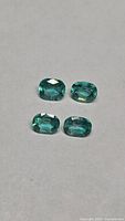Four cushion-cut emeralds under neutral lighting