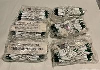 Six sealed plastic sleeves containing white-wire string lights with green bulb bases