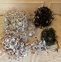 Tangled assortment of white, black, and green-wired mini string lights with red bulbs; spare bulbs bag visible