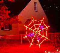 Night view of assembled illuminated orange spider web with purple spider outdoors