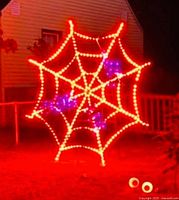 Assembled LED spider web lit in red/orange with purple spiders