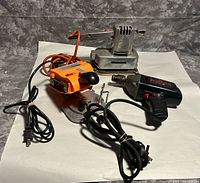 Overview of three corded power tools: metal sander, orange jigsaw, black drill