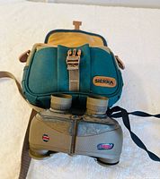 Binoculars positioned in front of teal Sierra gear bag showing overall lot contents