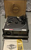 Top view of Kodak Carousel 550 projector with coiled remote cord, original box, and manual