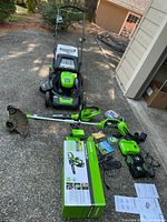 Lawn mower, blower, trimmer, batteries, chargers and manuals displayed on driveway