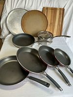 All items grouped: four Tramontina fry pans, Viking sauté pan, Viking saucepan with lid, two pizza pans, wood cutting board