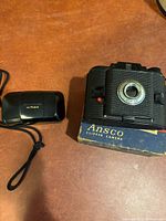Both cameras side by side: Olympus Stylus Infinity closed, Ansco Clipper on box fragment