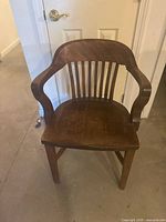 Front view of wooden banker’s chair showing seat, arms, and slat back