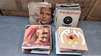 Four stacks of 45 rpm records with visible sleeves including Peggy Lee, Beatles, Queen “Body Language,” A&M label
