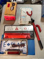 All items laid out: spot lamp box, steering lock, safety triangle kit, E Plate frame, maps