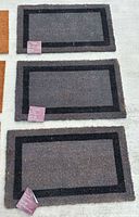 Three identical grey and black border coir mats on floor
