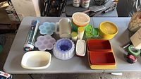 Overall layout of assorted Tupperware containers, silicone molds, pitcher, colander and decorator kit on table