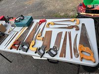 Table with multiple panel saws, backsaws, coping saw frame, saw blades, goggles, blue Makita case
