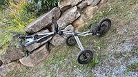 Full side view of folded Sun Mountain silver golf push cart against stone wall