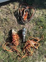 Overview of two work lamps with cords and coiled booster cables on grass