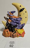 Front view of ceramic witch figurine on crescent moon with pumpkins and black cat