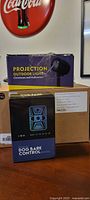 Three boxed products: projection outdoor light, dog bark control device, plain box for wall lamp