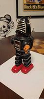 Front view of black tin Robby The Robot toy showing chest panel, red feet, single orange hand