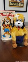 Front view of plush tin boxing dog beside box