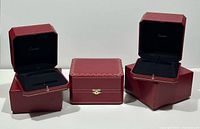 Three red Cartier jewellery boxes, two open showing interiors and sleeves