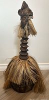 Front view showing horned face, serrated neck, raffia skirt and base
