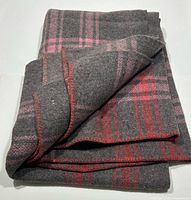 Folded grey wool blanket showing plaid pattern and red whipstitched edge