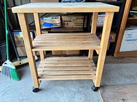 Front angled view of wooden cart showing top and two slatted shelves on casters