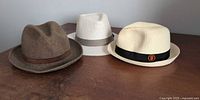 Three fedoras displayed on table: brown felt, cream with grey band, cream with black SF Giants band