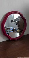 Front view of red-framed round mirror leaning against wall