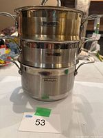 Stacked view of base pot, two steamer inserts and lid showing DeLonghi branding