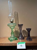 green glass hurricane lamp and two purple glass candle holders on shelf